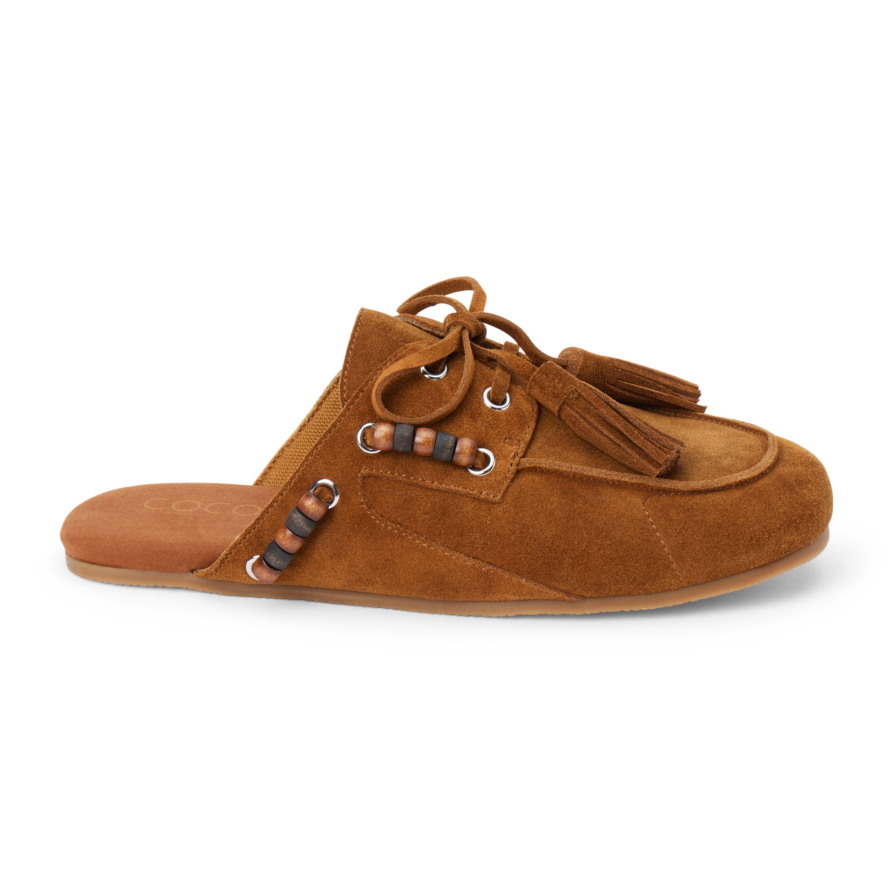Brown suede mule with an open back, moc-toe stitching, lace-up tassels, contrasting wood bead accents, and a flat sole shown on a white background.