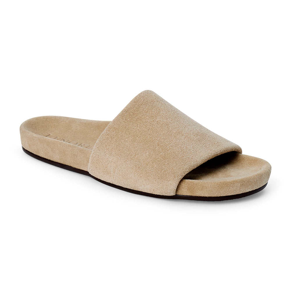 Sand beige suede flat slide sandal with wide strap and molded footbed, shown on a white background.