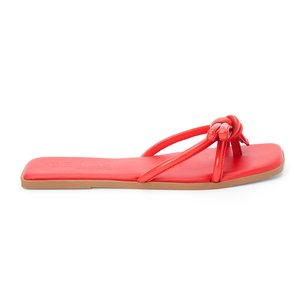 Red leather flat slide sandal with knotted straps and open toe, shown on a white background.