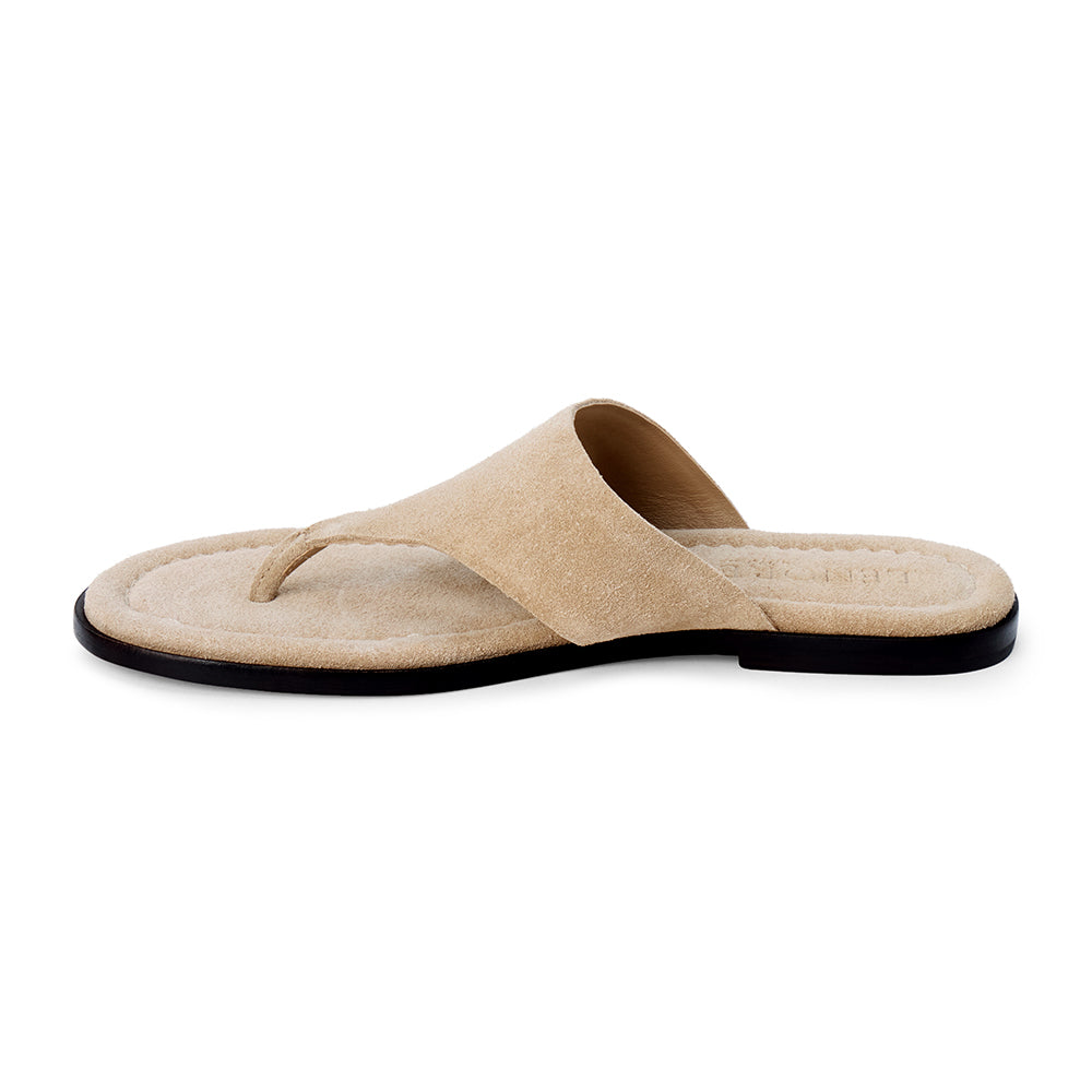 Sand beige suede flat thong sandal with wide strap and cushioned footbed, shown on a white background.