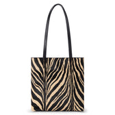 Black and tan cow hair tote bag with a zebra stripe pattern, rectangular body, and two long black shoulder straps shown on a white background.