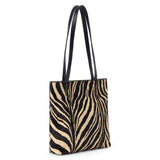 Black and tan cow hair tote bag with a zebra stripe pattern, rectangular body, and two long black shoulder straps shown on a white background.