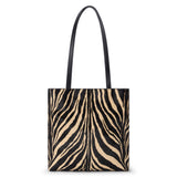 Black and tan cow hair tote bag with a zebra stripe pattern, rectangular body, and two long black shoulder straps shown on a white background.