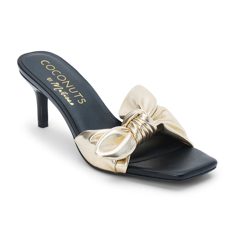 Uptown Vegan Heeled Mule – Coconuts by Matisse – Gold metallic slip-on sandal with square toe, bow detail strap, and tapered kitten heel.