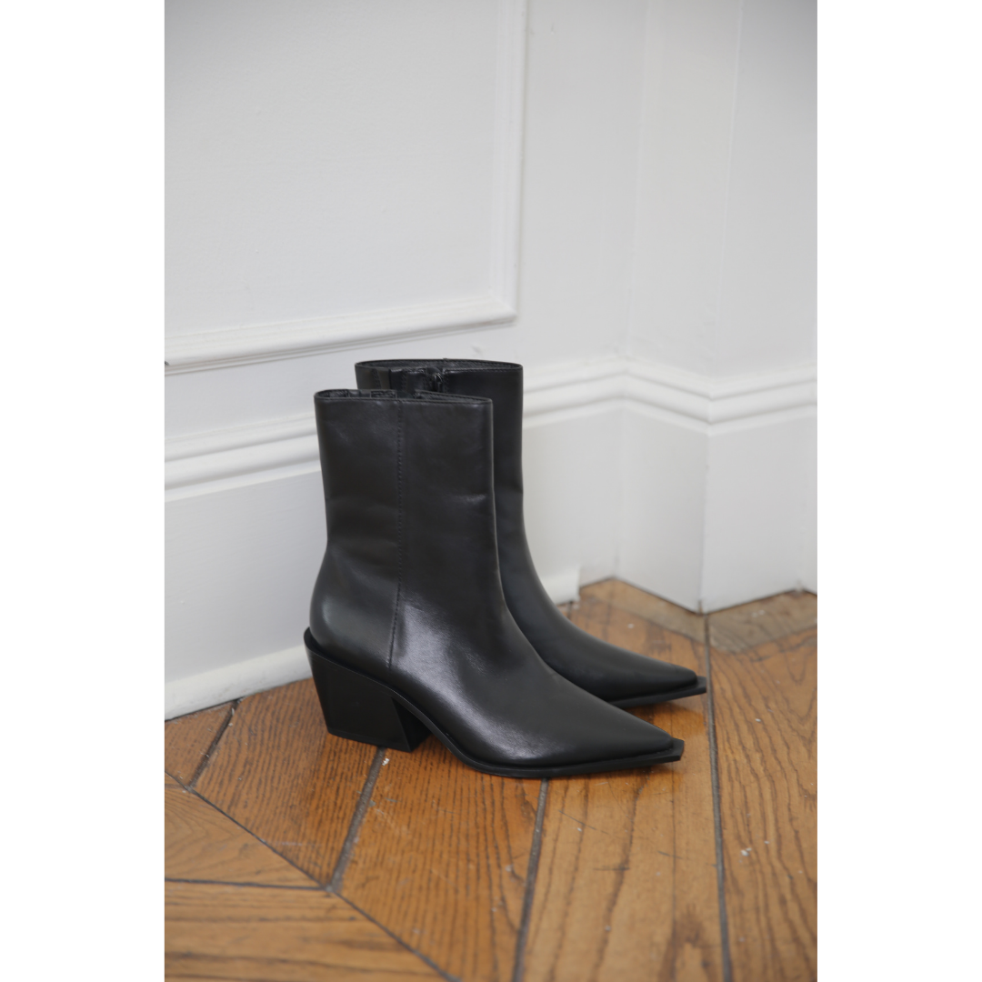Pair of black leather ankle boots on a wooden floor against a white wall.