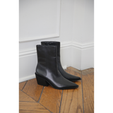Pair of black leather ankle boots on a wooden floor against a white wall.