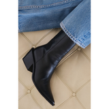 Black ankle boots worn with blue jeans on a beige tiled floor