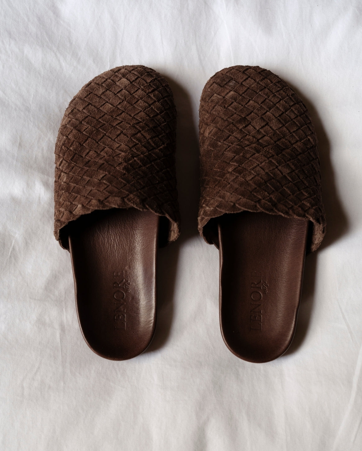 Pair of brown woven mules on a white background