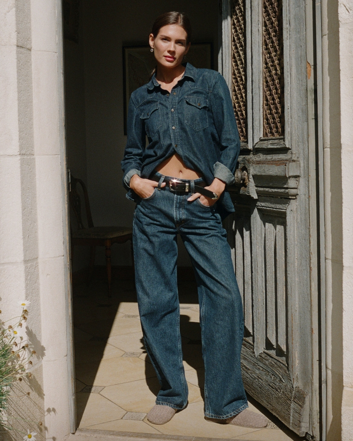 Woman wearing a denim outfit standing in a doorway.