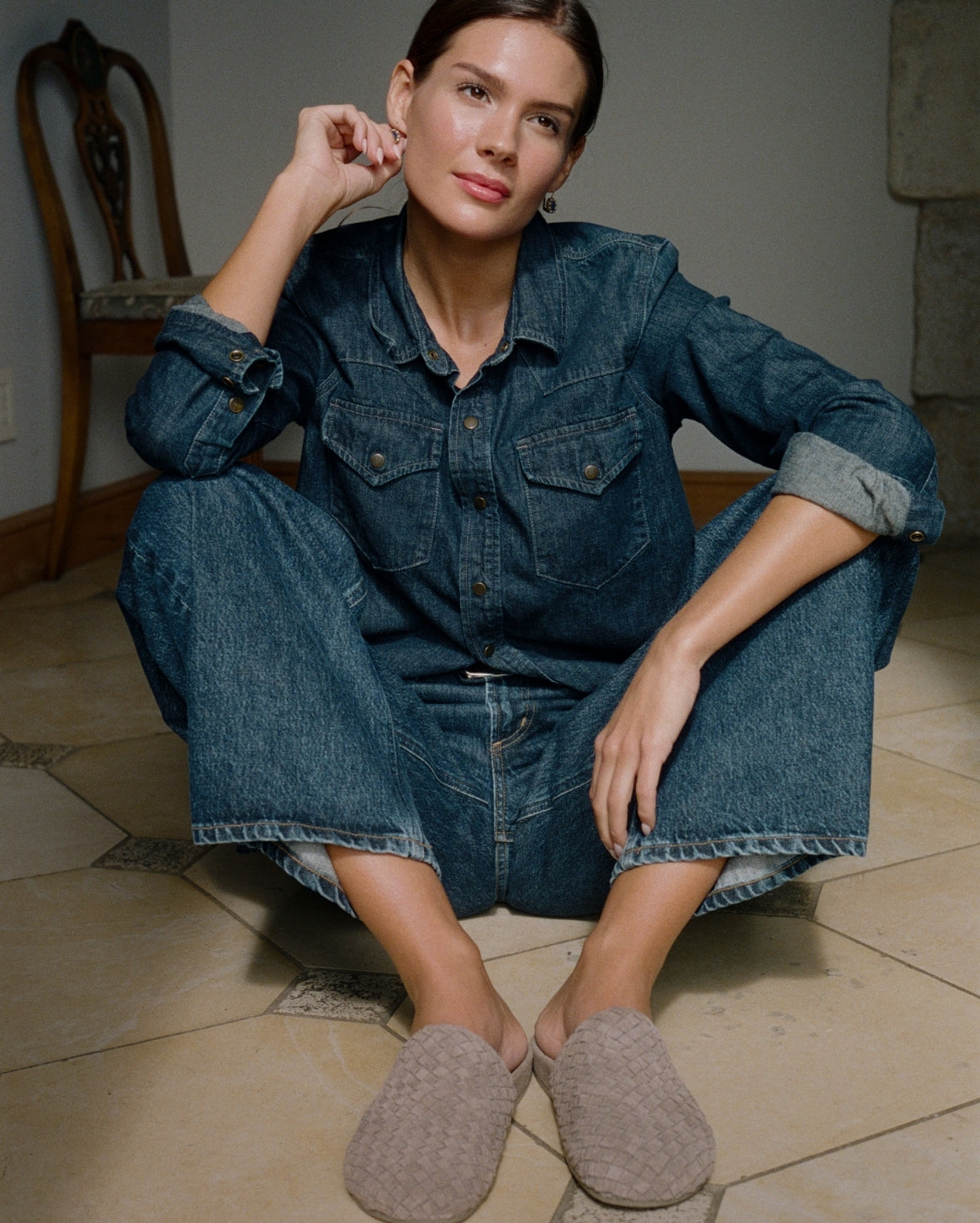 Woman wearing a denim dress sitting on the floor with beige slip-on shoes.