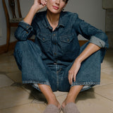 Woman wearing a denim dress sitting on the floor with beige slip-on shoes.