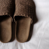 A pair of brown woven slip-on shoes with a suede-like footbed, laid flat on a white fabric background. The brand name 'LENORE' is debossed on the footbed.