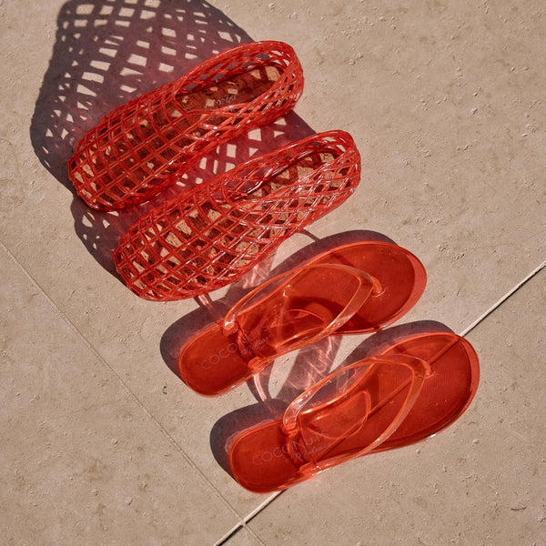 Olsen red jelly flip-flops and Marlow red woven jelly flats with transparent straps and a minimalist design. A lightweight, water-friendly essential for effortless summer wear.