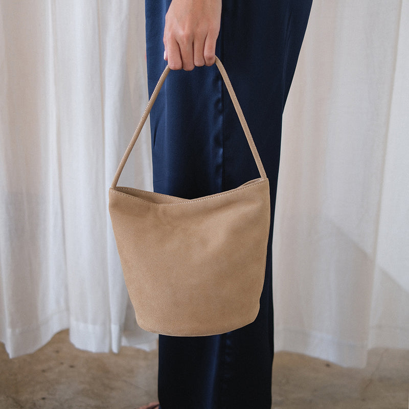 Vancouver Bucket Bag - Matisse Footwear - Minimalist bucket bag in soft beige colored suede with a seamless silhouette and a single shoulder strap. A versatile and unstructured carryall with effortless, elevated appeal.