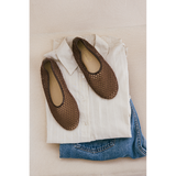 Brown woven ballet flats on a white shirt and blue jeans with a beige background.