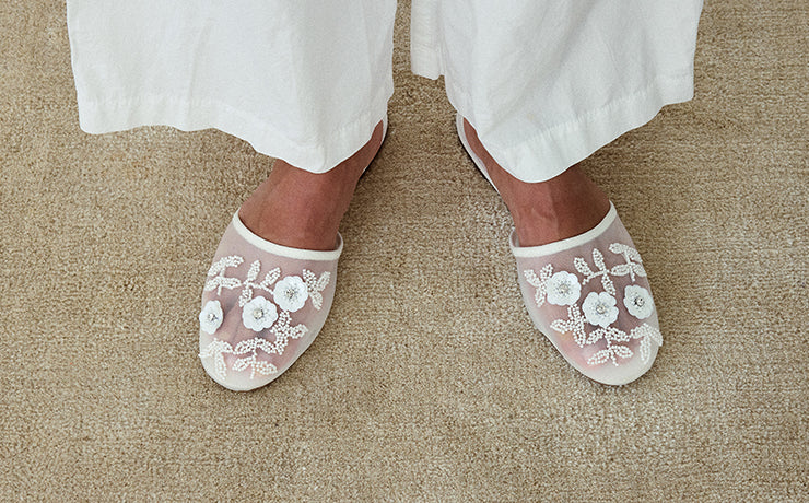 White embroidered Maven mule worn with white pants on a beige carpet.