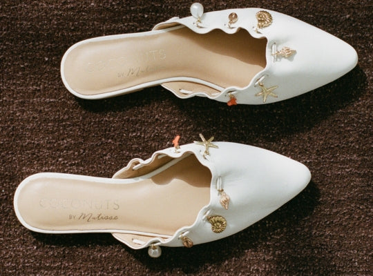 Pair of white shoes with decorative embellishments on a brown surface