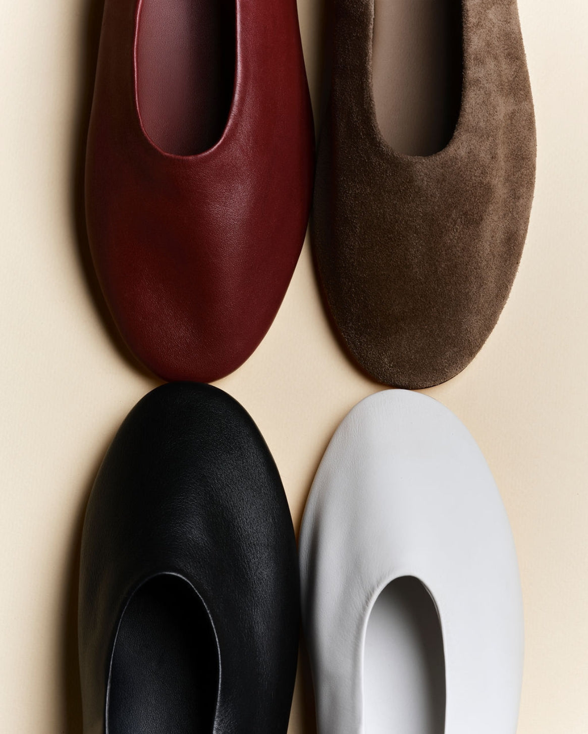 Four minimalist slip-on flats arranged in a 2x2 grid on a light beige background, showing different color options: burgundy leather, brown suede, black leather, and white leather.