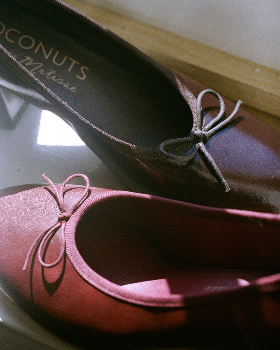 A pair of women's low-heeled flats in a deep burgundy red fabric, featuring a small matching fabric bow on the toe. The insole of the upper shoe displays the brand name 'Coconuts by Matisse'.