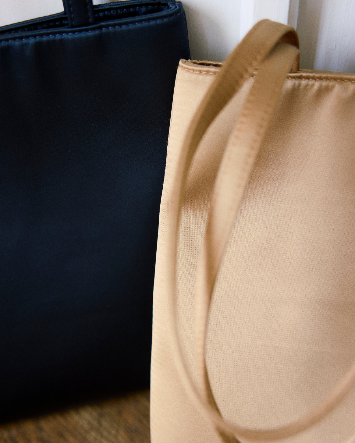 Close-up of a golden satin tote bag in the foreground with its strap draped over the side, next to a dark navy tote bag, against a white background.
