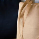 Close-up of a golden satin tote bag in the foreground with its strap draped over the side, next to a dark navy tote bag, against a white background.