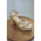 Beige paltform sandal with a block heel on a wooden surface.