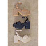 Three pairs of chunky platform block-heeled sandals in brown, black, and beige on a textured surface.
