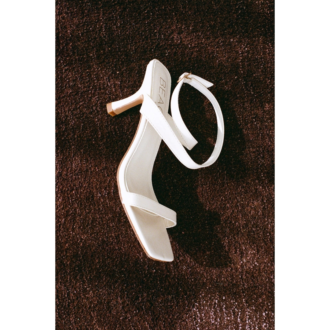 White high-heeled sandal on a brown carpet.