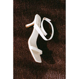 White high-heeled sandal on a brown carpet.