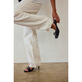 Person wearing beige pants and black heeled sandals against a white background.