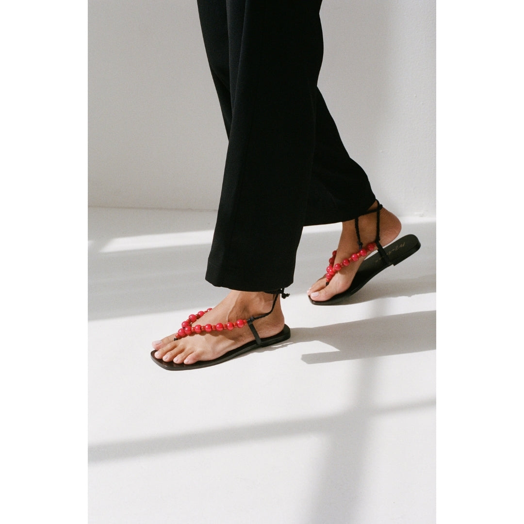 Black thong sandals with red beading worn by a person on a white background.