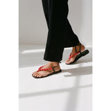 Black thong sandals with red beading worn by a person on a white background.