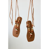 Pair of brown sandals with beaded straps hanging against a light gray background.