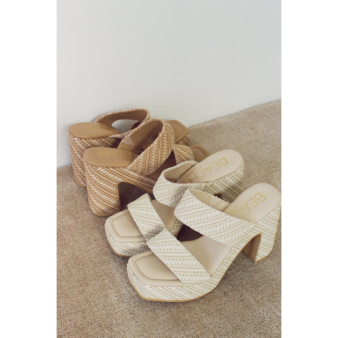 Two pairs of woven high-heeled platform sandals on a textured surface with a neutral background,