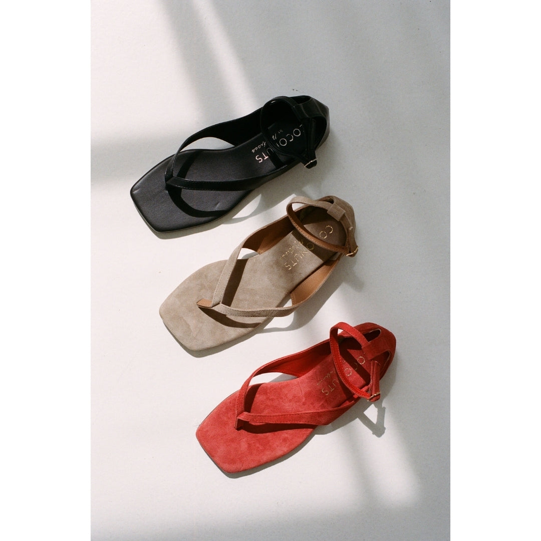 Three pairs of sandals in black, brown, and red on a light gray background.