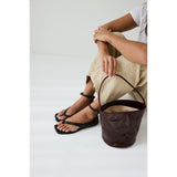 Person wearing black sandals holding a brown leather bucket on a white background.