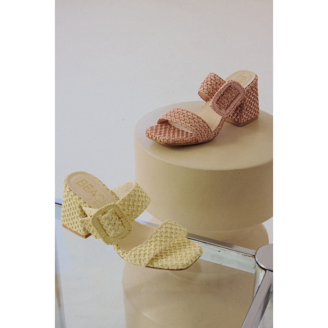 Two paisr of woven high-heeled sandals on a beige stand with a white background.
