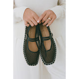 Person holding a pair of black mesh Mary Jane flats with a white background.