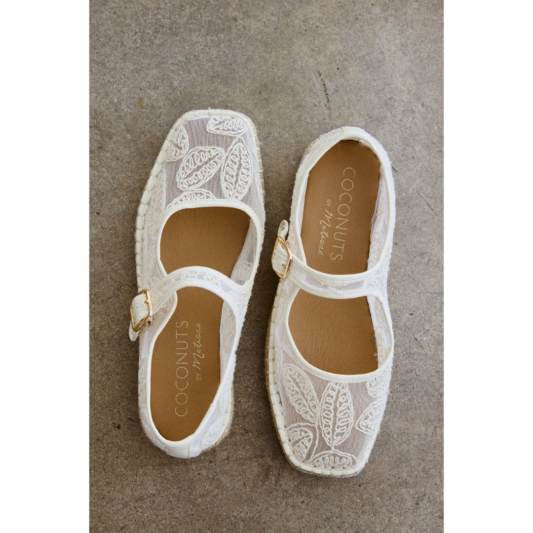 Pair of white lace Mary Jane flats with 'Coconuts' branding on a concrete surface.
