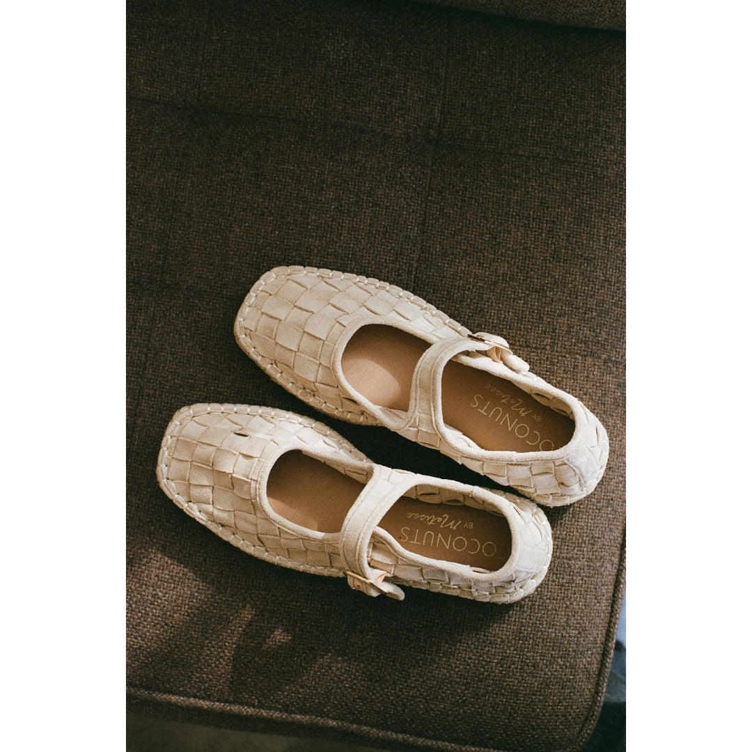 Pair of woven Mary Jane flats on a brown textured surface.