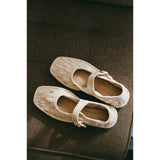 Pair of woven Mary Jane flats on a brown textured surface.