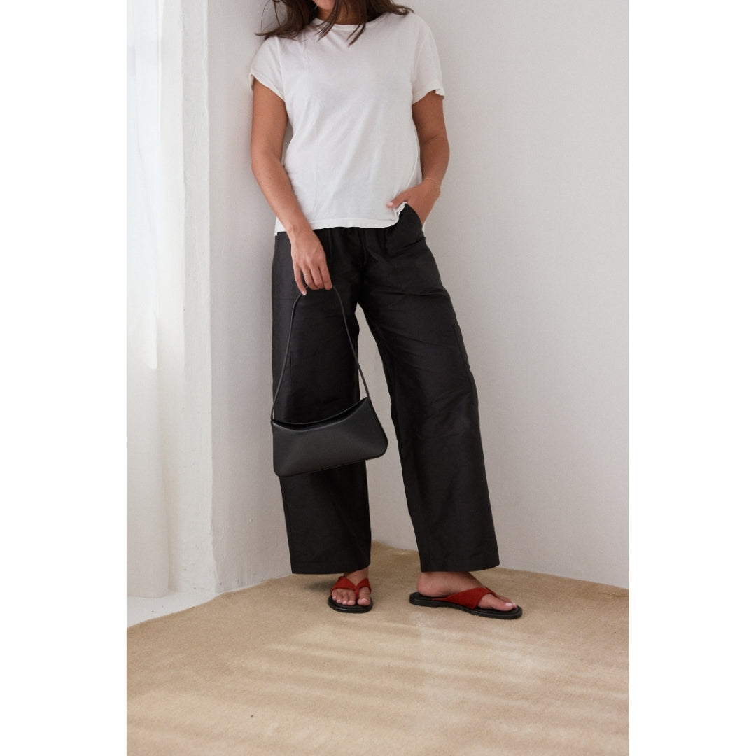 Person wearing a white t-shirt and black wide-leg pants holding a black bag indoors.