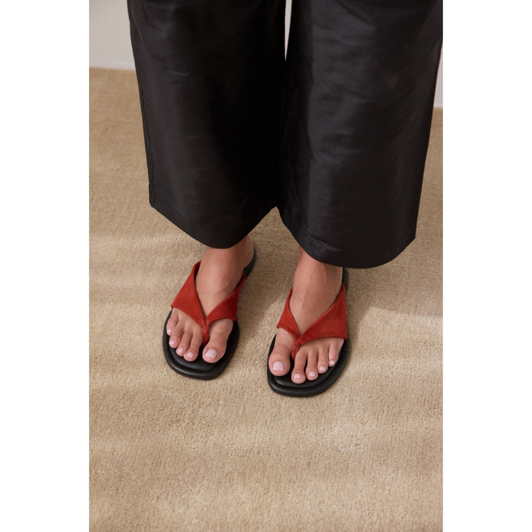 Person wearing red sandals with black soles on a beige carpet.