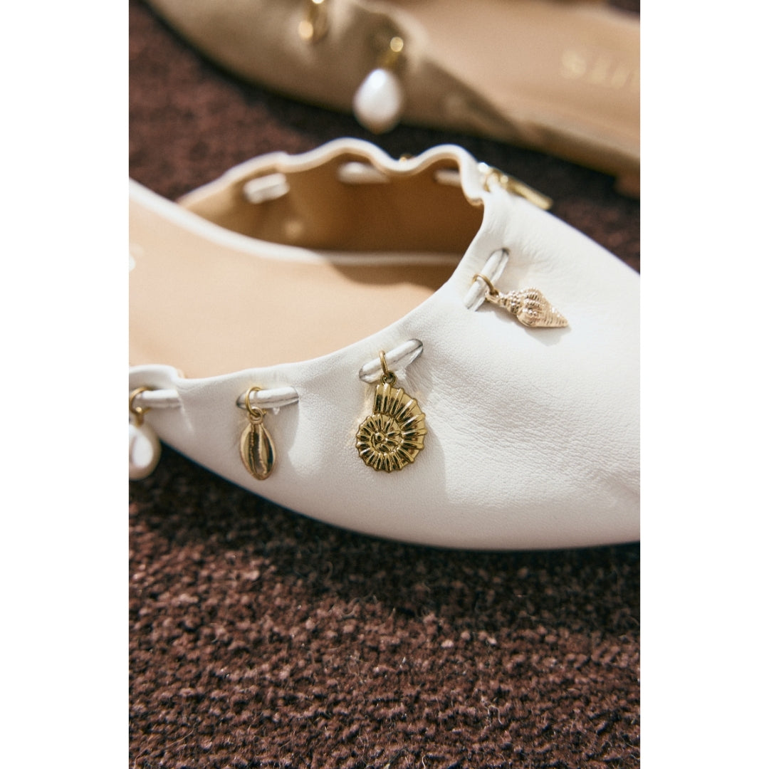 Close up of a white shoe with gold charms on a textured brown surface.