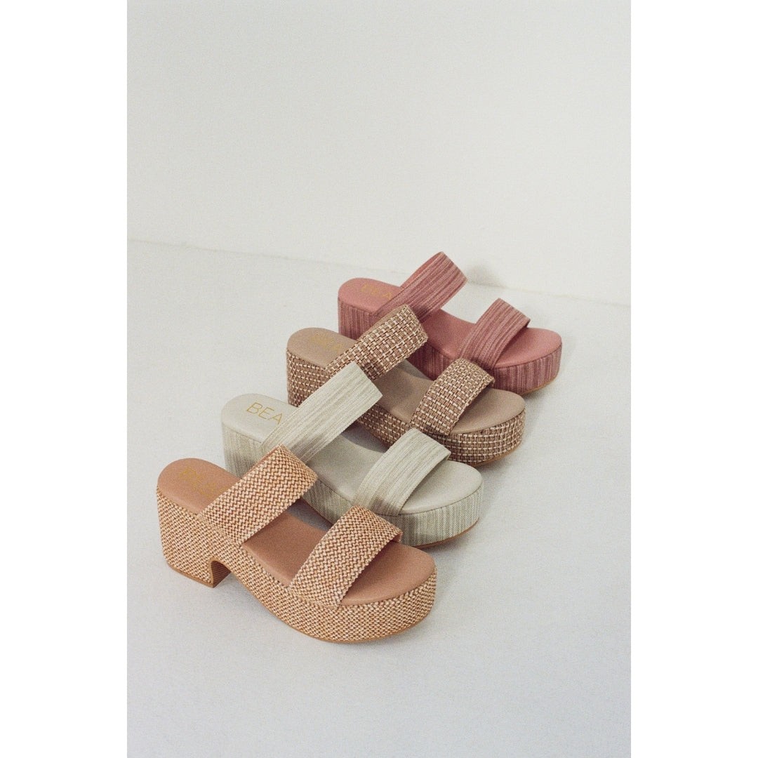 Four high-heeled platform sandals in pink, brown, grey and tan on a light gray background.