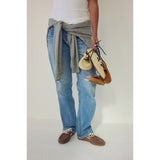Person wearing blue jeans and a gray sweater, holding shoes against a white background.