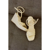 Pair of light yellow wedge sandals on a textured surface.