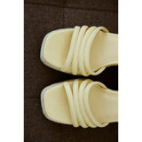 Pair of light yellow sandals on a brown surface.