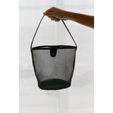 Hand holding black mesh handbag against a white background.