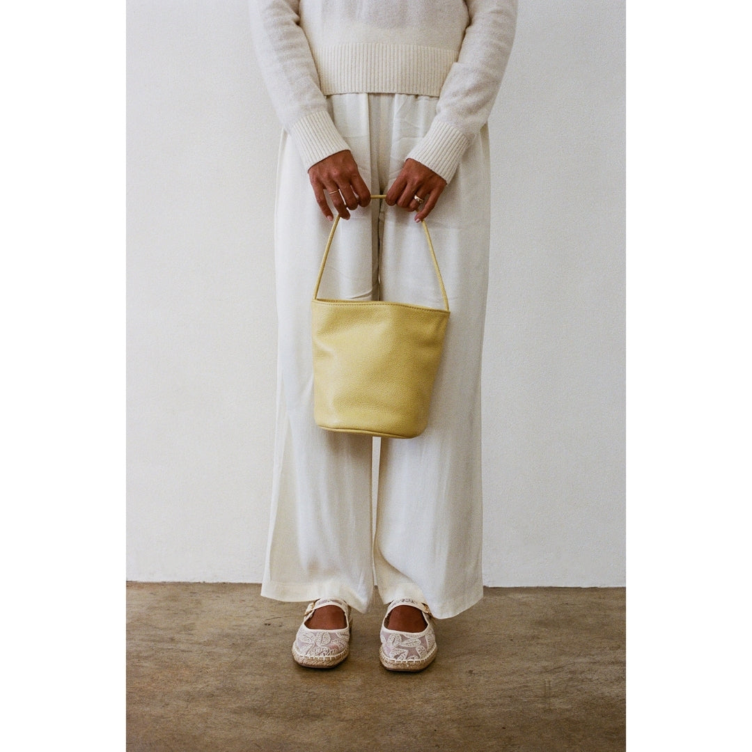 Person holding a yellow bag wearing a white outfit against a plain background.